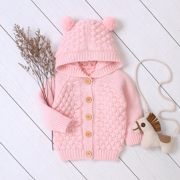Pink knitted baby outfit with a hat and toy on a white wooden floor